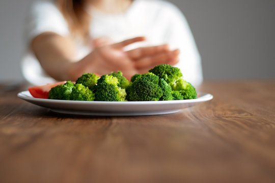 No vegan diet concept. Teen girl pushing away plate with broccoli and other vegetables refusing to eat. Food waste. Copy space. Selective focus on food.