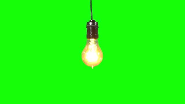 Light bulb hanging in the studio and glowing with bright light. Shot in 4k resolution with green screen background