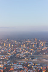 Vertical view of misty cityscape with buildings and houses lighten by golden sunrise sun and rooftops covered by first snow