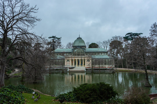 View of the glass palace in Retiro Park in Madrid, on a cloudy day at dawn, with ducks walking on the grass, travel concept.