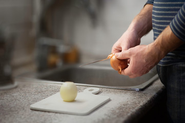 Men's hands with a sharp knife peeling white onions in the kitchen. Healthy food, vegetarian products.