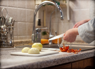 Work in the kitchen. Peeled white onions on a white cutting board, against the background of onion husks and women's hands washing a sharp knife under a stream of water. Healthy food, natural, 