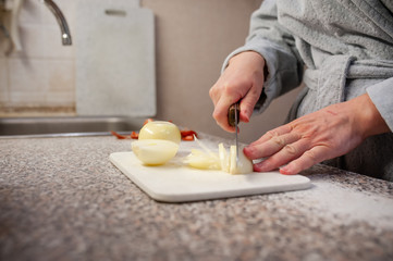 Women's hands cuting white onions with a knife on a cutting Board in the kitchen. Non-personalized....