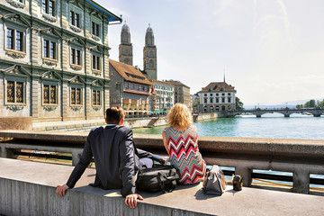 Romantic couple sitting at Limmat River Quay and looking at Grossmunster Church in Zurich, Switzerland