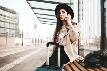 Fototapeta premium Stylish girl dressed in a coat and hat talking on the phone when waiting for public transport