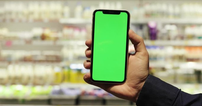 Close up of the black vertical smartphone with chroma key screen in Caucasian male hand while he taking pictures in the milk and dairy section in the shop. Indoor.