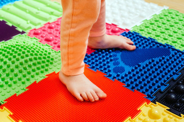 kid feet while standing on special massaging and orthopedic mat, close up. leg disease prevention...