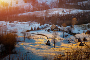 Winter holiday landscape in rural area, old house and snow covered haystacks at sunset