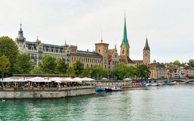 Fototapeta premium Zurich, Switzerland - September 2, 2016: Restaurant terrace at Limmat River quay and Saint Peter Church and Fraumunster Church in the city center of Zurich, Switzerland.