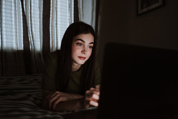 Smiling young european woman lying on sofa at home, working distantly on computer. chatting with friends in social networks, studying online, surfing information.