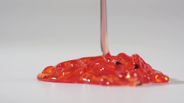 Red gel flowing on the table and slowly lay down on the flatness. Light white background in studio room. Detailed view in 4k.