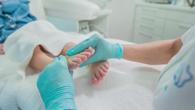 Professional foot reflexologist gently massages baby foot of patient toddler