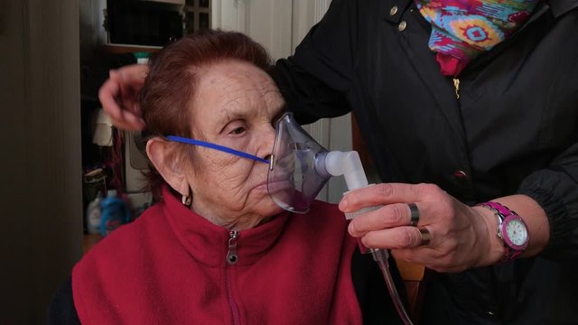 Woman placing mask for medicinal treatment on the face of an elderly woman