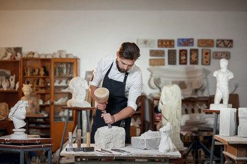 Stone carver works with wooden hammer and chisel at limestone.