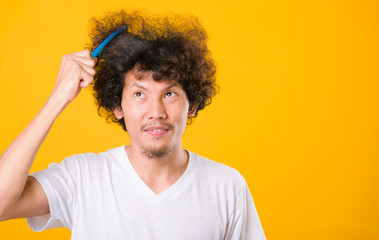 Asian man combing curly hair on yellow background