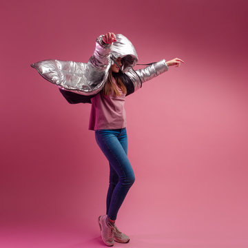 Fashionable And Modern Young Woman In A Puffy Light Down Jacket Throws A Hood Over Her Head.