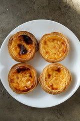 Four portuguese pasteis of cake with custard on white plate on textured background