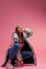 A cool girl in a shiny silver down jacket and a knitted hat squatted down,