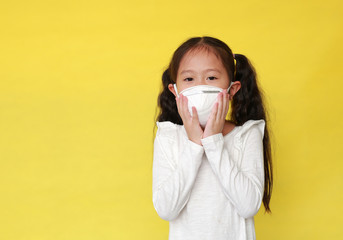 Portrait of asian little child girl wearing a protection mask for against air pollution isolated on yellow background. Kid with health care concept.