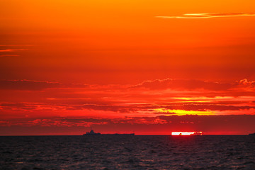 Merchant ships on the horizon against the background of a fiery red sunset
