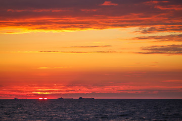 Merchant ships on the horizon against the background of a fiery red sunset