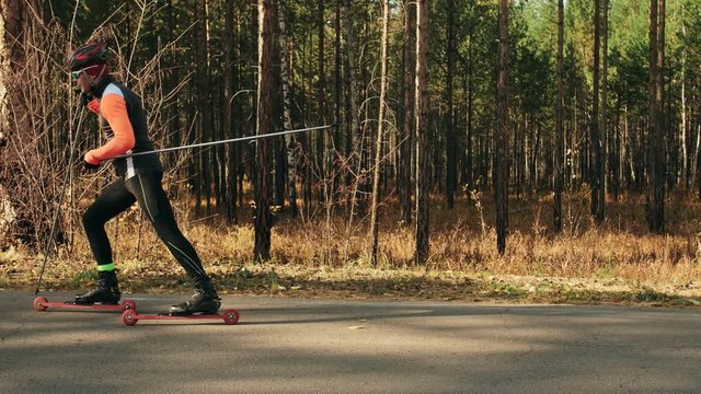 Training an athlete on the roller skaters. Biathlon ride on the roller skis with ski poles, in the helmet. Autumn workout. Roller sport. Adult man riding on skates. The athlete shows the basics of