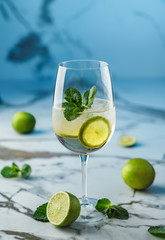 Fresh Mojito cocktail with lime, mint and ice in wineglass on light blue background. Summer cold drink and cocktail