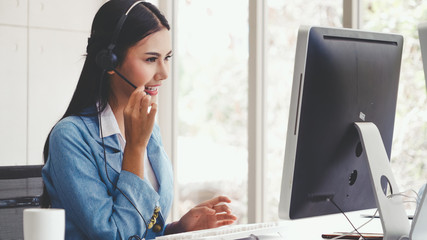 Customer support agent or call center with headset works on desktop computer while supporting the...