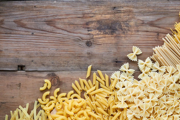 Different types of raw pasta on old wooden background