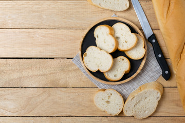 Sliced baguettes on wooden dish with knife on the wooden table.