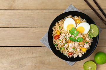 Bowl of instant noodle with minced chicken and boiled egg on wooden table.