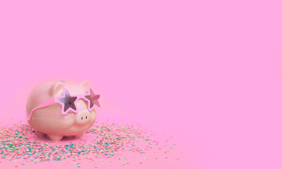 A pink piggy bank in fun glasses at a party. Pink background.