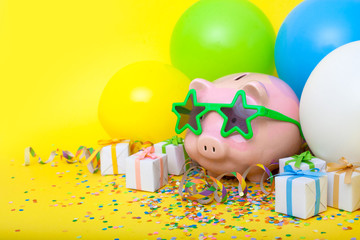 A pink piggy bank in fun glasses at a party, confetti, gift. Yellow background.