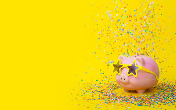 A pink piggy bank in fun glasses at a party. Yellow background.