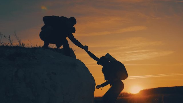 Couple hiking help each other silhouette in mountains. Teamwork couple hiking, help each other, trust assistance, sunset. Man giving hand a woman to help her to climb the mountain.