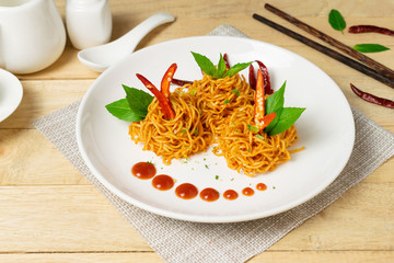 Instant noodles with dry chili and tomato sauce in white dish on wooden table.