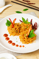 Instant noodles with dry chili and tomato sauce in white dish on wooden table.