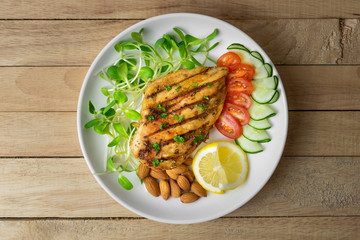 Top view of Fresh salad with chicken breast in white dish on wooden table, Almond,Sunflower seedling,Cucumber,Tomato,Lemon.