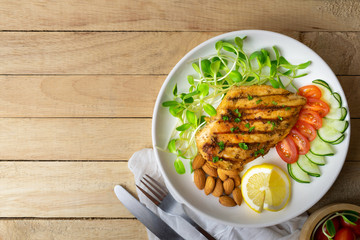 Top view of Fresh salad with chicken breast in white dish on wooden table, Almond,Sunflower seedling,Cucumber,Tomato,Lemon.