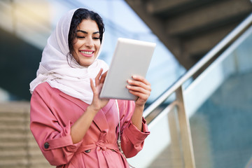 Young Arab woman wearing hijab using digital tablet outdoors