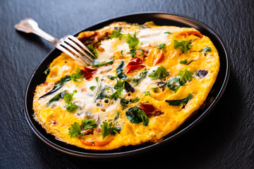 Breakfast - scrambled eggs with vegetables on black stone background