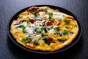 Breakfast - scrambled eggs with vegetables on black stone background