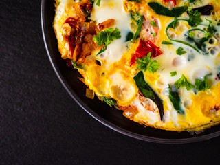 Breakfast - scrambled eggs with vegetables on black stone background