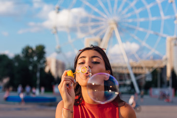 Beautiful young woman blowing soap bubbles outdoors