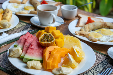 Tropical breakfast of fruit, coffee and scrambled eggs and banana pancake for two on the beach near sea