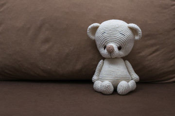 Fototapeta premium A small white knitted bear on a soft sofa.
