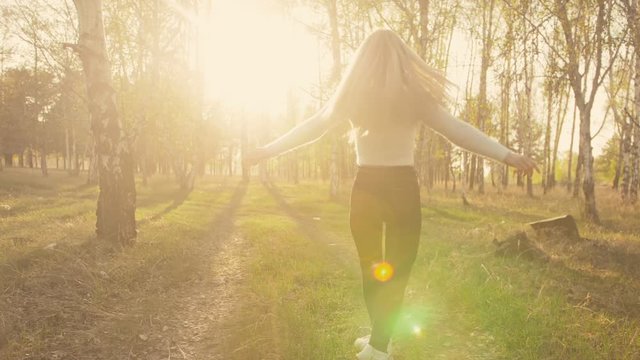 Attractive young woman in sweater, jeans is dance and spinning among blossom apple tree. Sunset, spring orchard and green field. Slow motion. Caucasian one girl, long fluttering hair. Sun glasses.