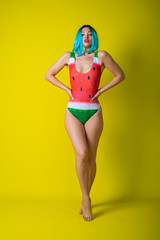 Portrait of a woman in a swimsuit with a picture of a watermelon. Stylish girl in a colored short wig posing in the studio on a yellow background.