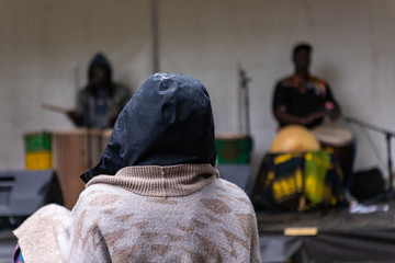 Closeup rear view of person wearing raincoat and listening music playing by two artists during event in rainy season. at world and spoken word festival