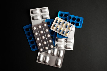 Different tablets, pills in foil blister packs, medications drugs on black background